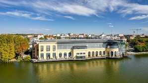 A waterfront building with a glass facade, a covered outdoor area, and a view of the cityscape in the background.