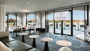 A modern hotel lobby with seating areas, tables, and large windows offering views of a lake.