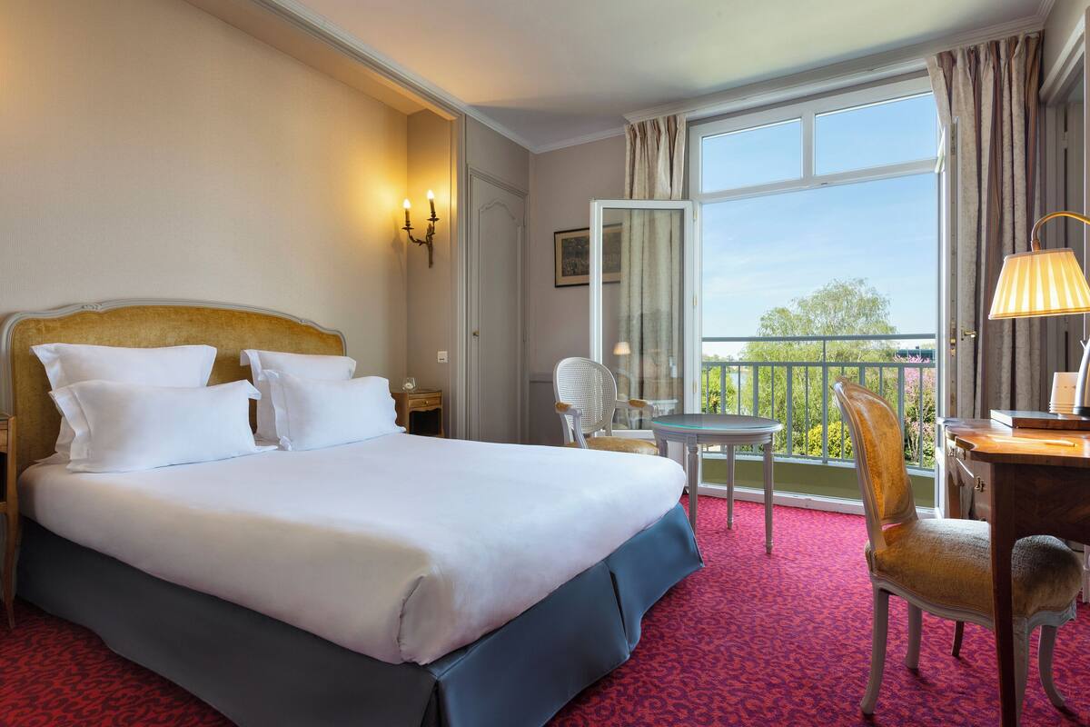 Quarto de hotel com cama grande, escrivaninha, cadeira e varanda com vista.