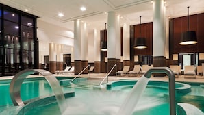 A modern indoor pool area with clear water, lounge chairs, and a central water feature.