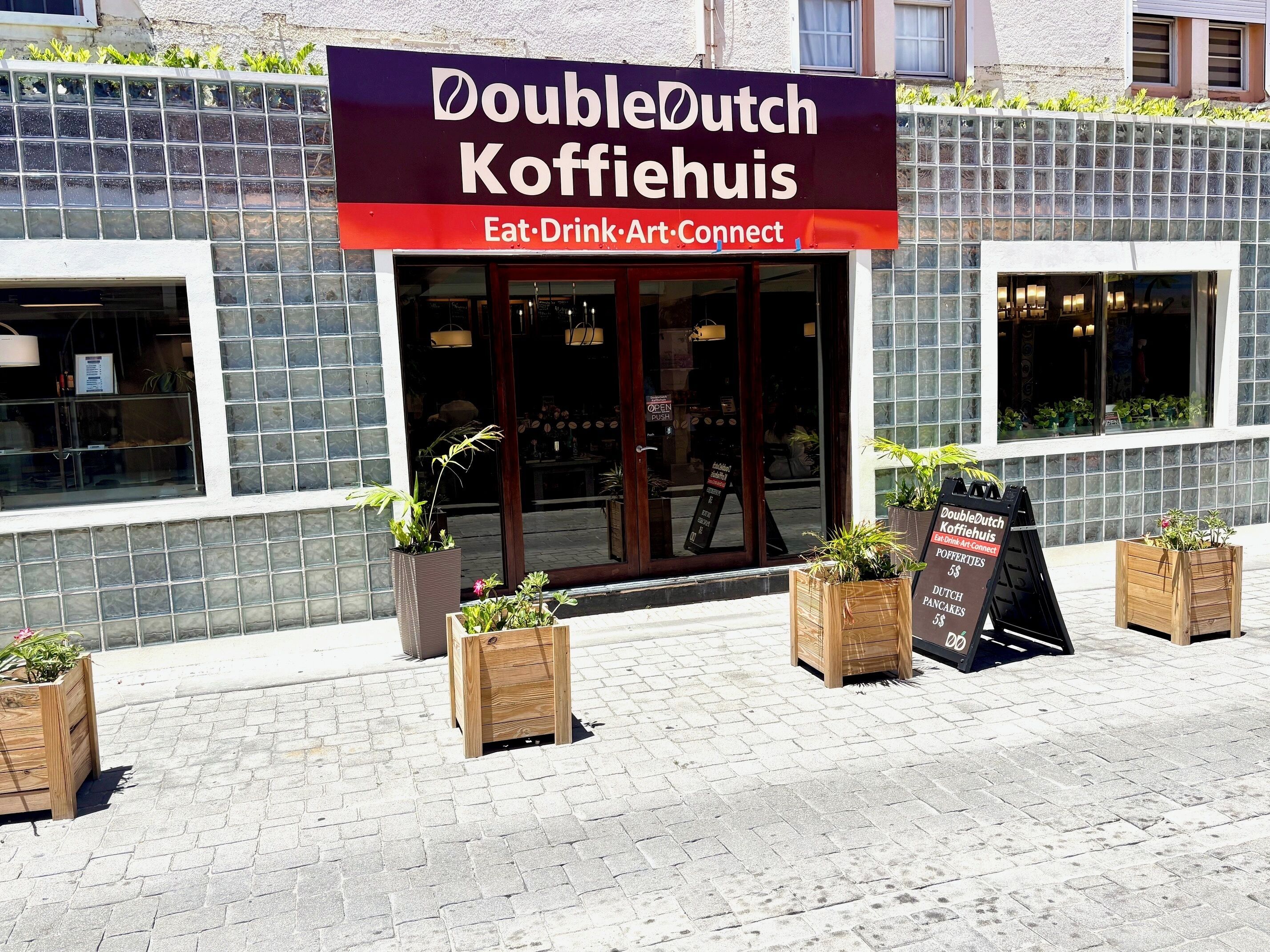 A DoubleDutch Koffiehuis storefront with a signboard, potted plants, and a brick-paved sidewalk.