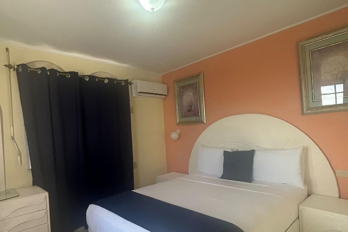 A bedroom with a bed, a nightstand, a dresser, a window with curtains, and an air conditioning unit.