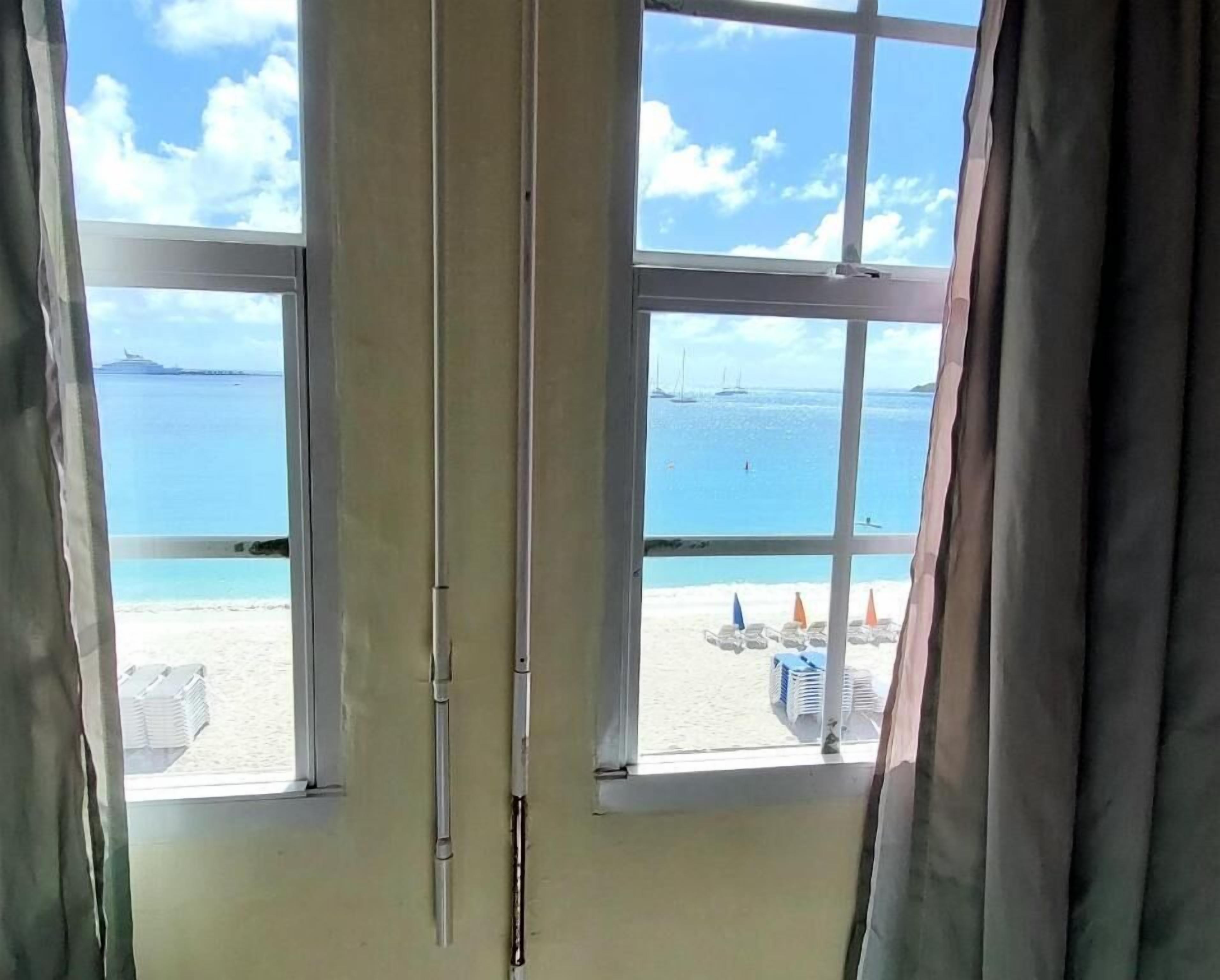 Una habitación con un ventanal grande que da a una playa, con vistas claras al mar y una isla distante.