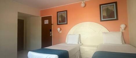 A hotel room with two beds, a small table, and a door leading to another room.