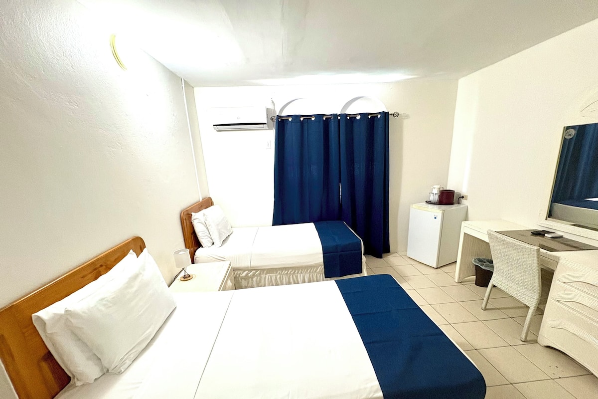 A hotel room with two beds, a desk, a chair, a small refrigerator, and a television.