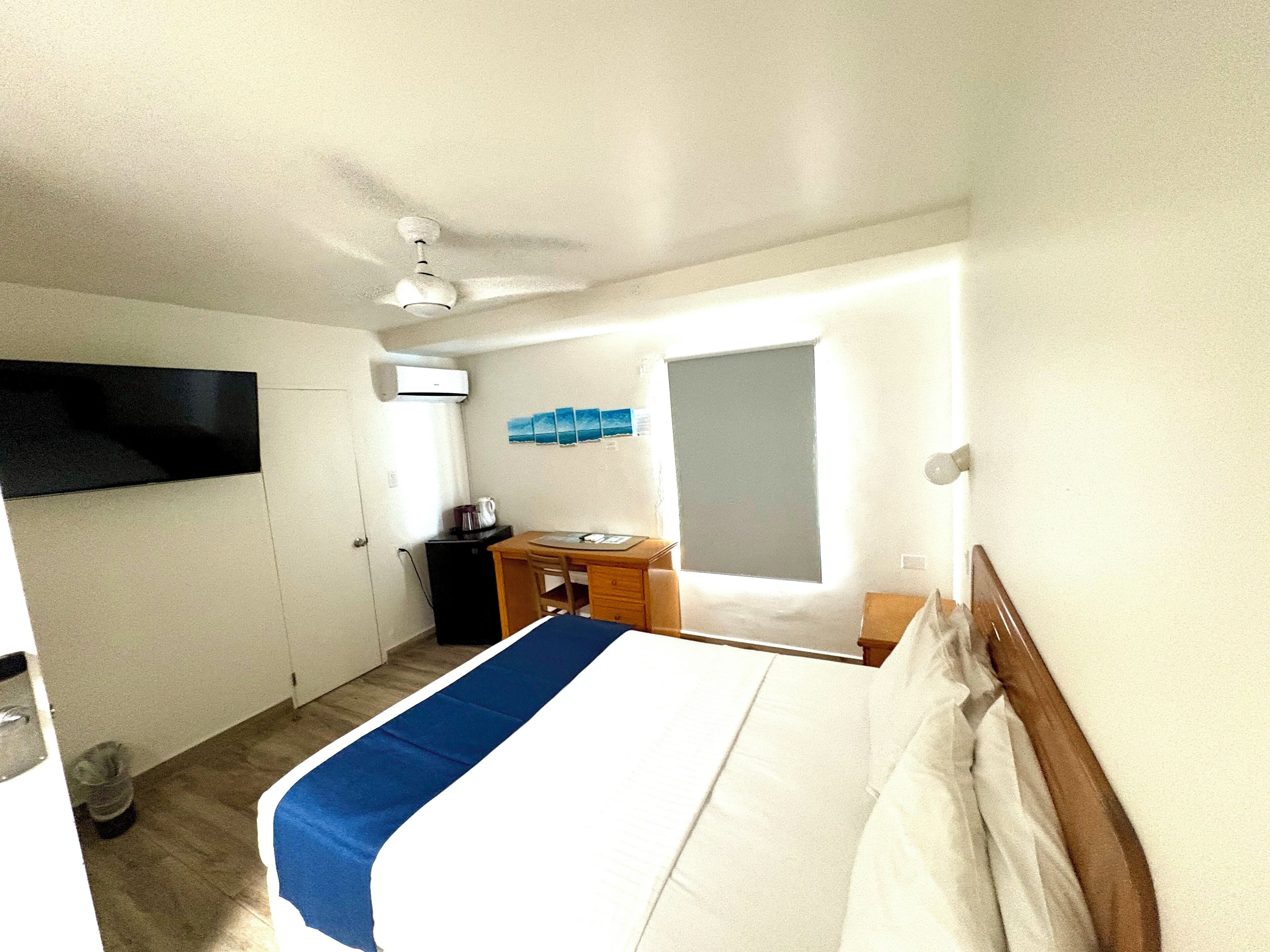 Habitación de hotel con cama, escritorio, silla, mesita con tetera y ventana con persianas.
