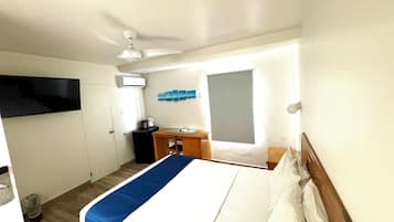 Habitación de hotel con cama, escritorio, silla, mesita con tetera y ventana con persianas.
