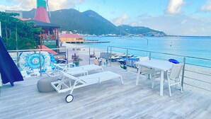 A deck with lounge chairs and tables overlooking a marina and mountains.
