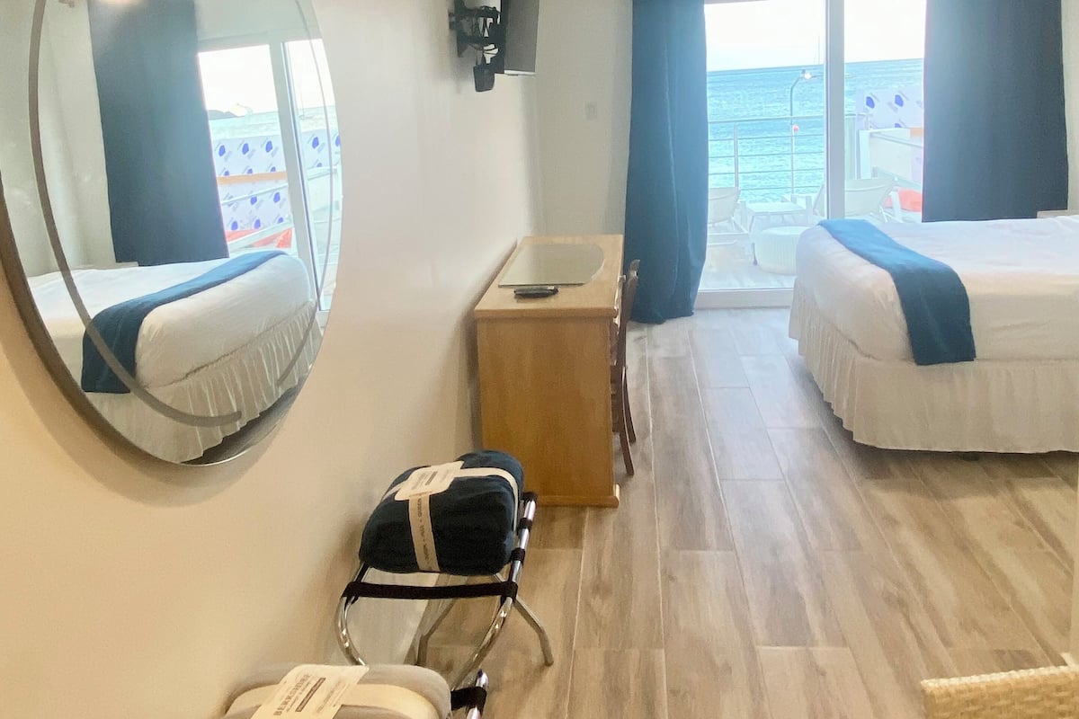 A hotel room with a bed, a desk, a chair, a mirror, and a view of the sea.