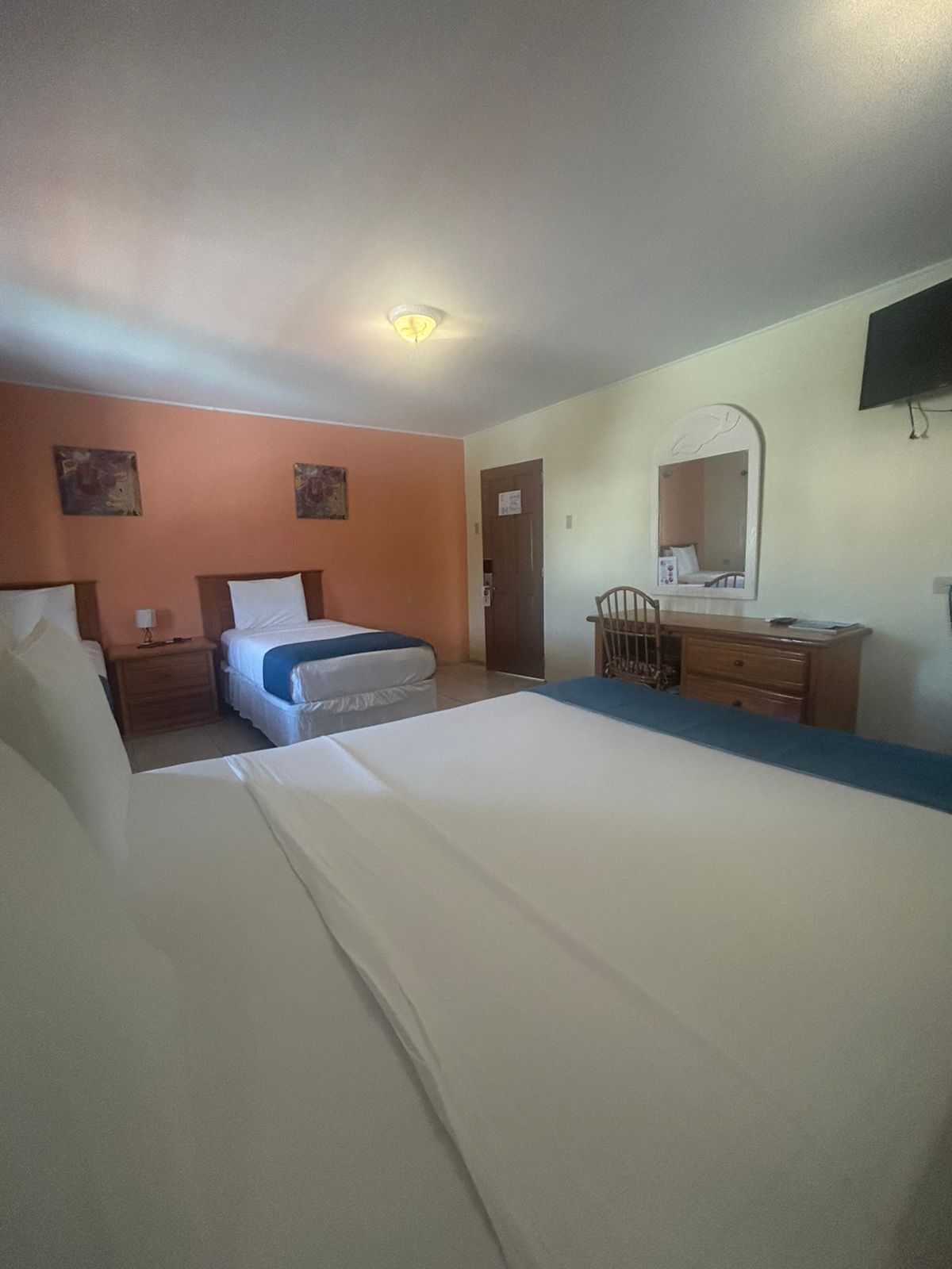 Ein Hotelzimmer mit einem großen Bett, einem Schreibtisch mit Stuhl, einem Schminktisch, einem Spiegel und einem an der Wand befestigten Fernseher.
