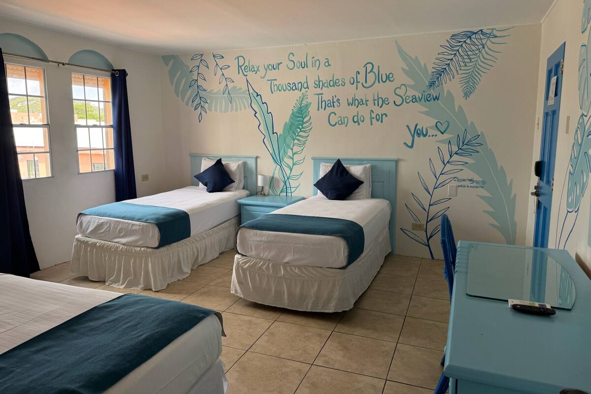 A room with two beds, a small table, and a wall mural with a calming message.