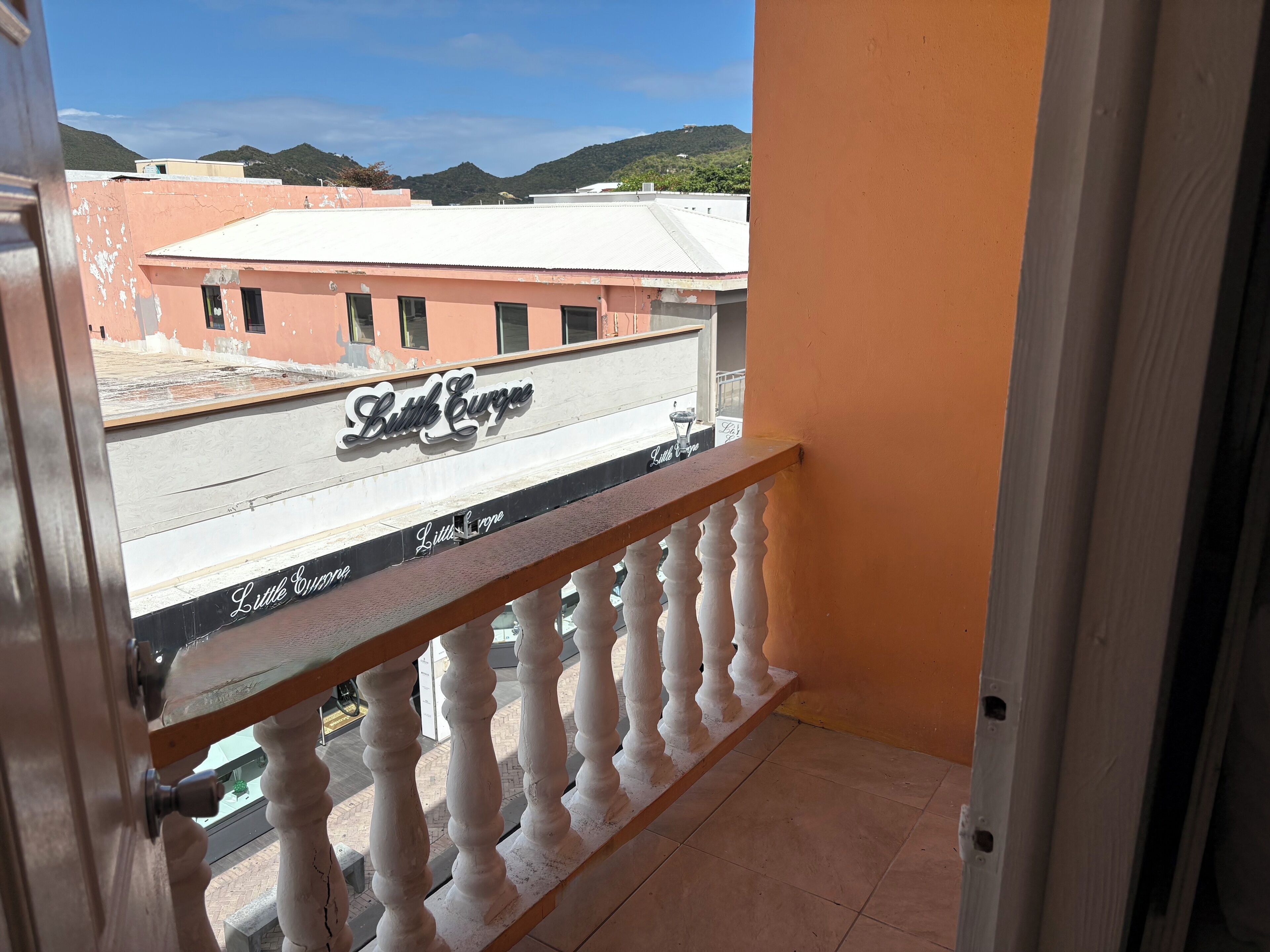 A balcony with a view of a building named 'Little Curve' and a mountainous landscape in the background.