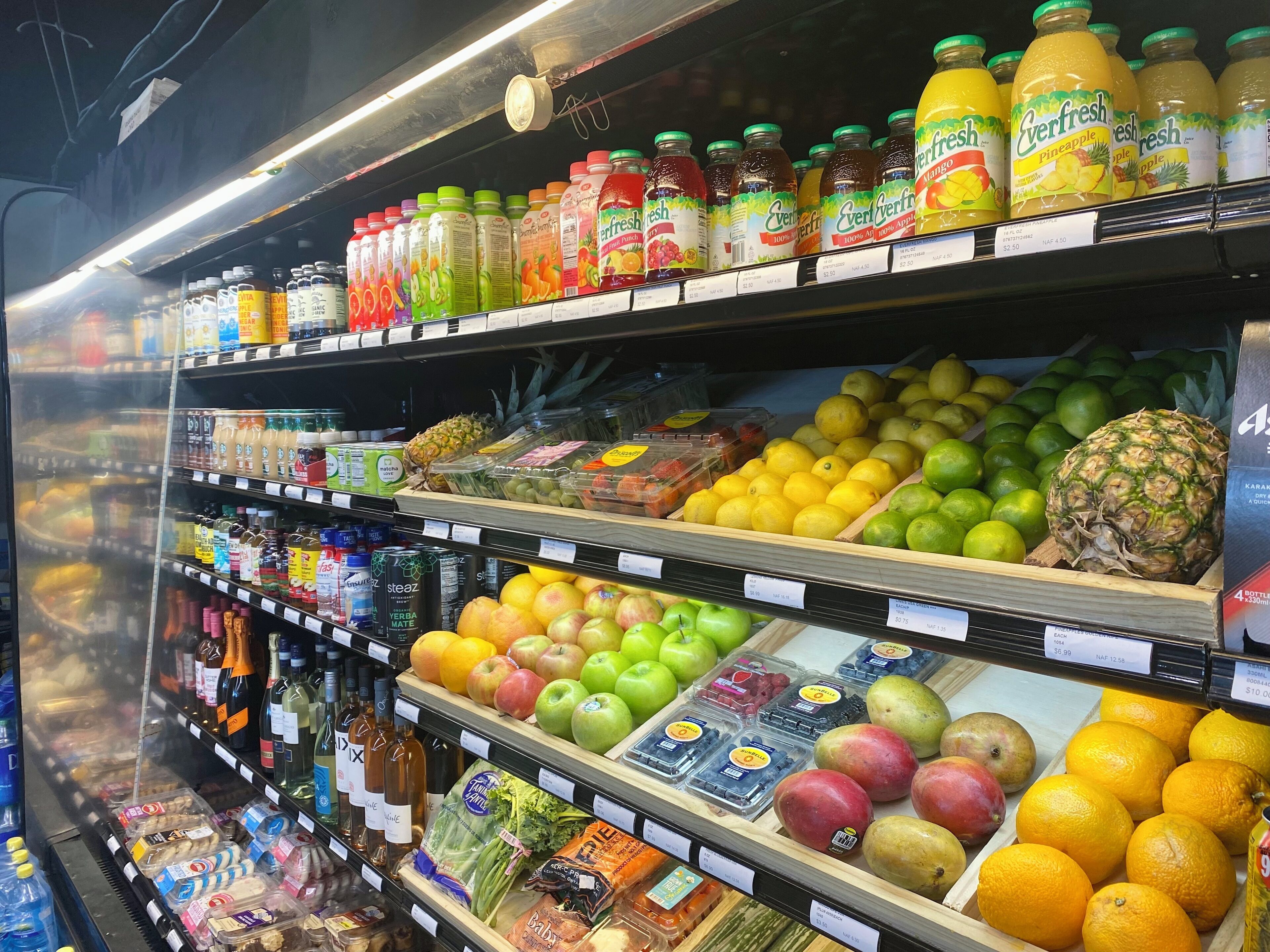 Le rayon des fruits et légumes et des boissons d’un supermarché, où l’on trouve une variété de fruits, de légumes et de boissons en bouteille.