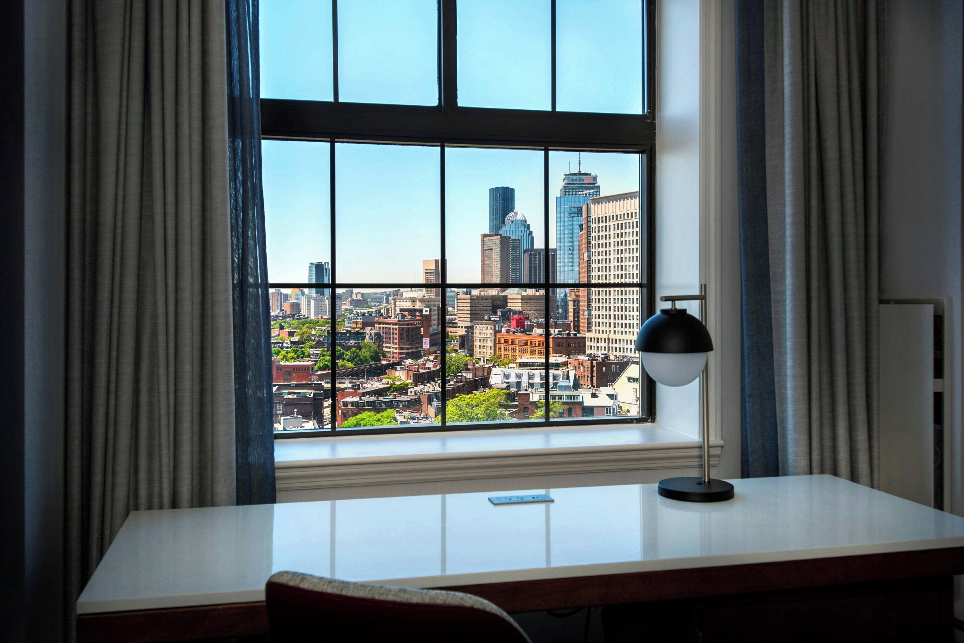 A room with a large window, a desk, a chair, and a lamp.
