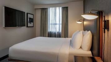 Une chambre d’hôtel avec un grand lit, une table de chevet, une lampe fixée au mur et une fenêtre avec des rideaux.