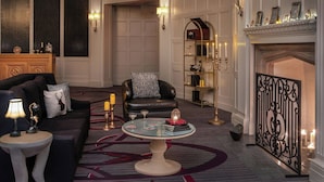 Un salon luxueux avec un canapé en cuir noir, une table basse ronde sur laquelle sont posées des jeux de cartes, une cheminée et un paravent décoratif.