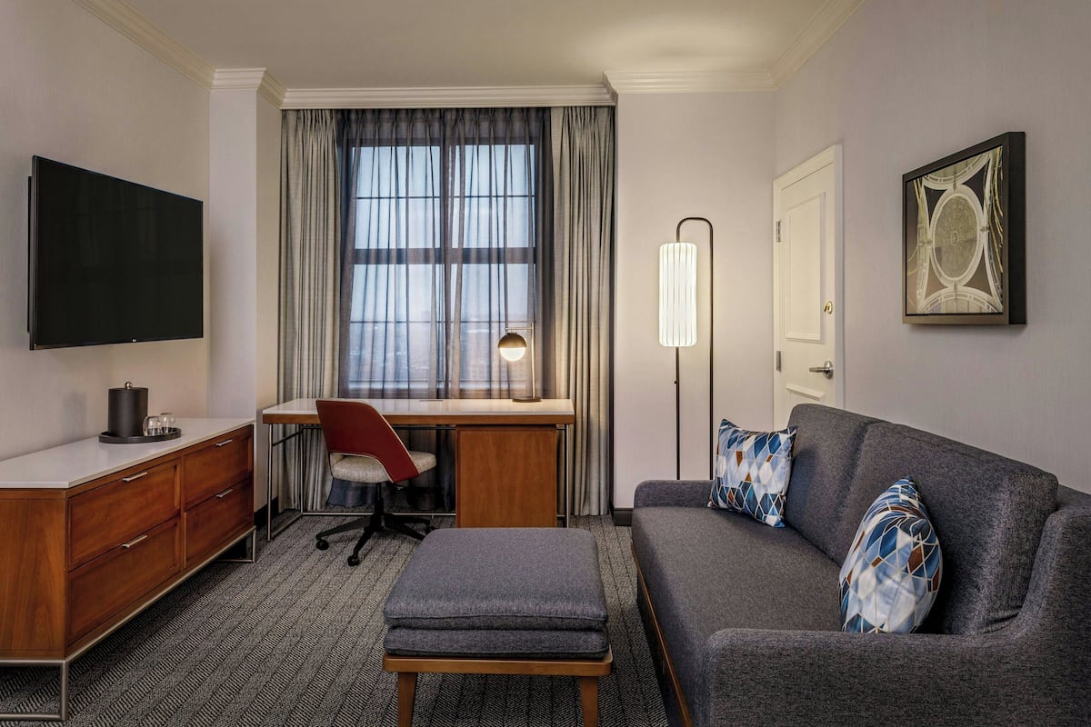 Quarto de hotel com escrivaninha, cadeira, televisão, sofá e obras de arte.