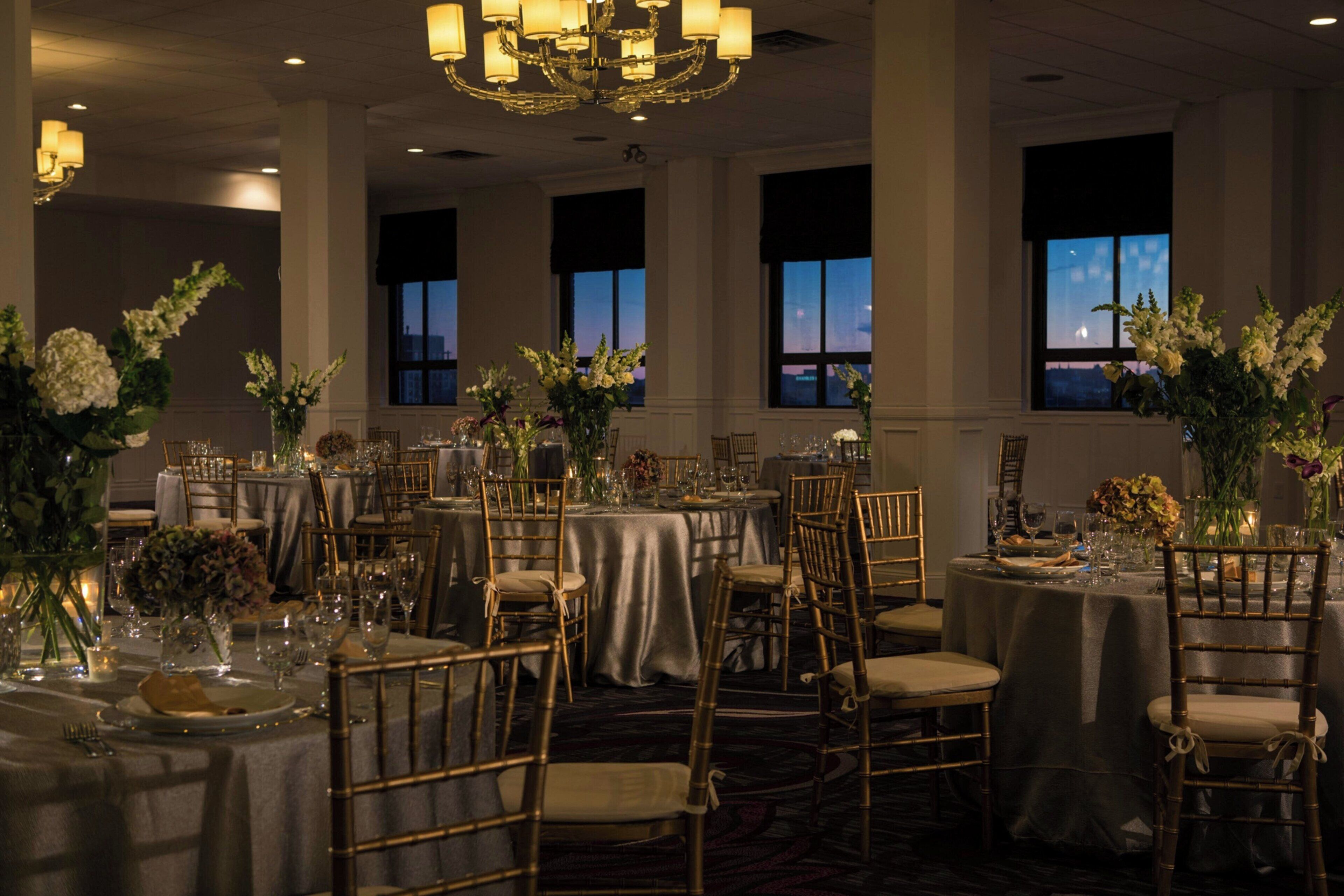 A banquet hall with round tables, gold chairs, and floral centerpieces.