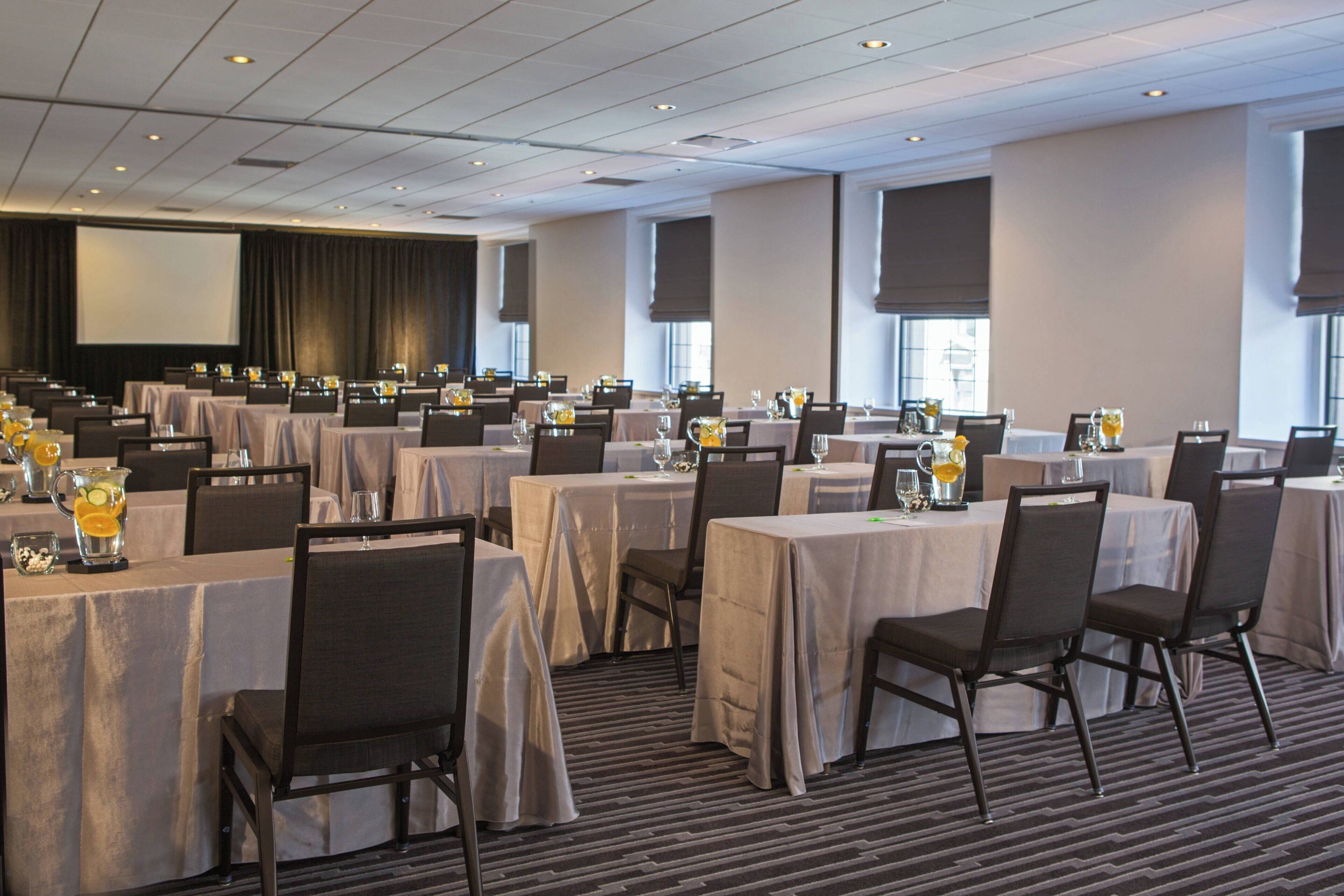 Un salón de conferencias con varias mesas, sillas y una pantalla grande al frente.
