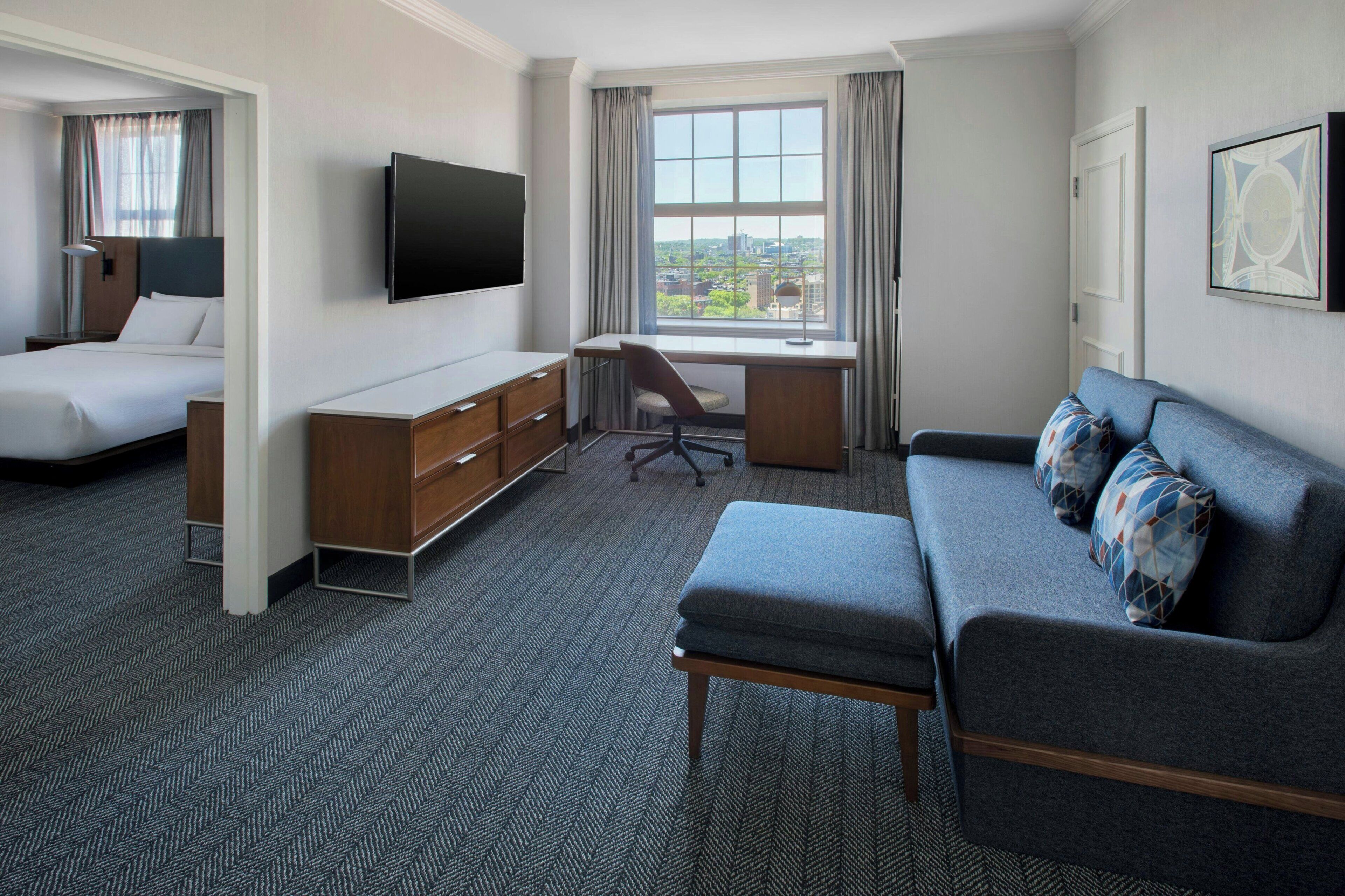 A hotel room with a bed, a desk, a chair, a sofa, and a TV.