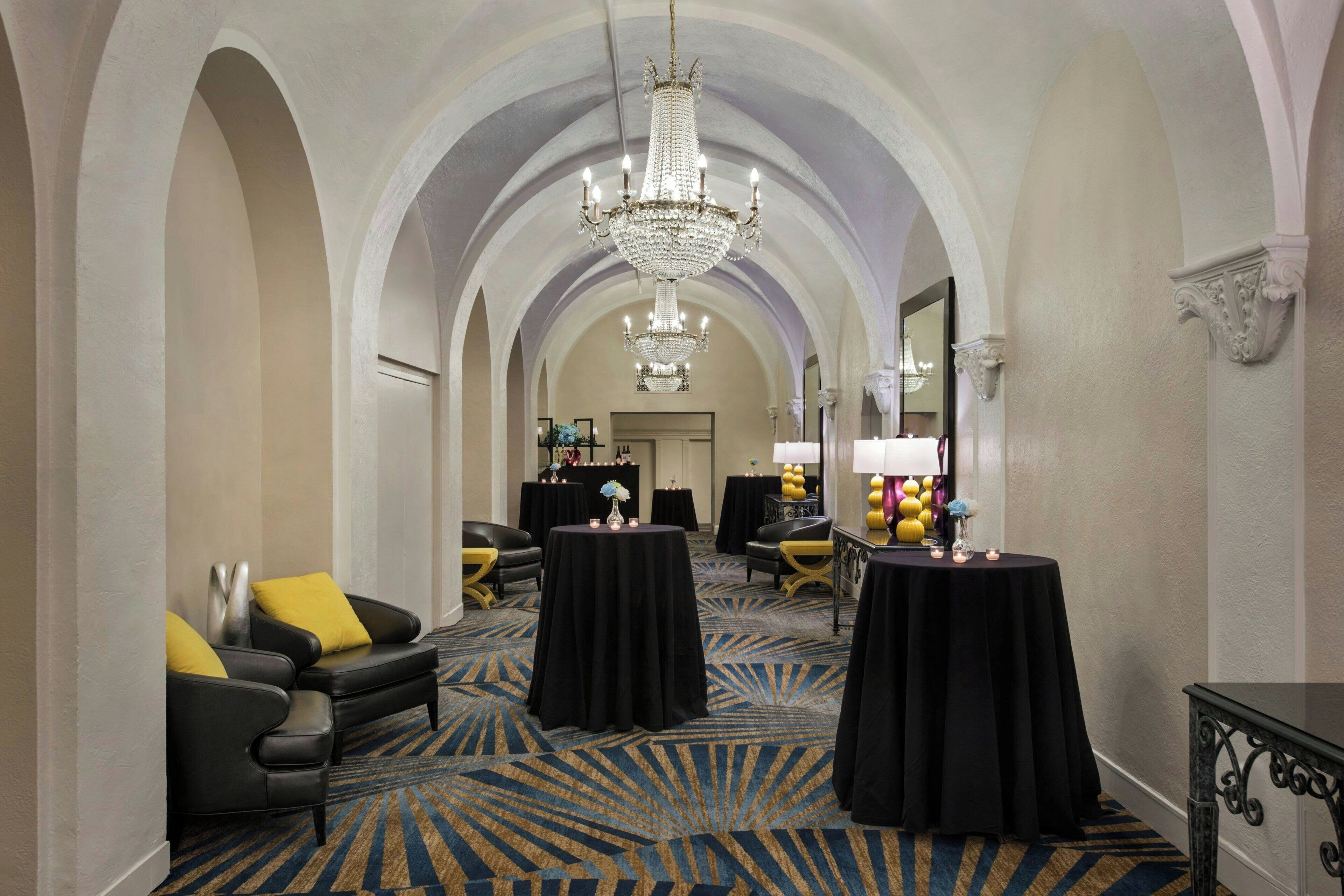 A hotel lobby with a grand chandelier, black and yellow seating, and a patterned carpet.