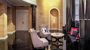Un hall d’entrée avec un sol en marbre, une porte blanche, deux fauteuils, une table ronde et un canapé avec des coussins.