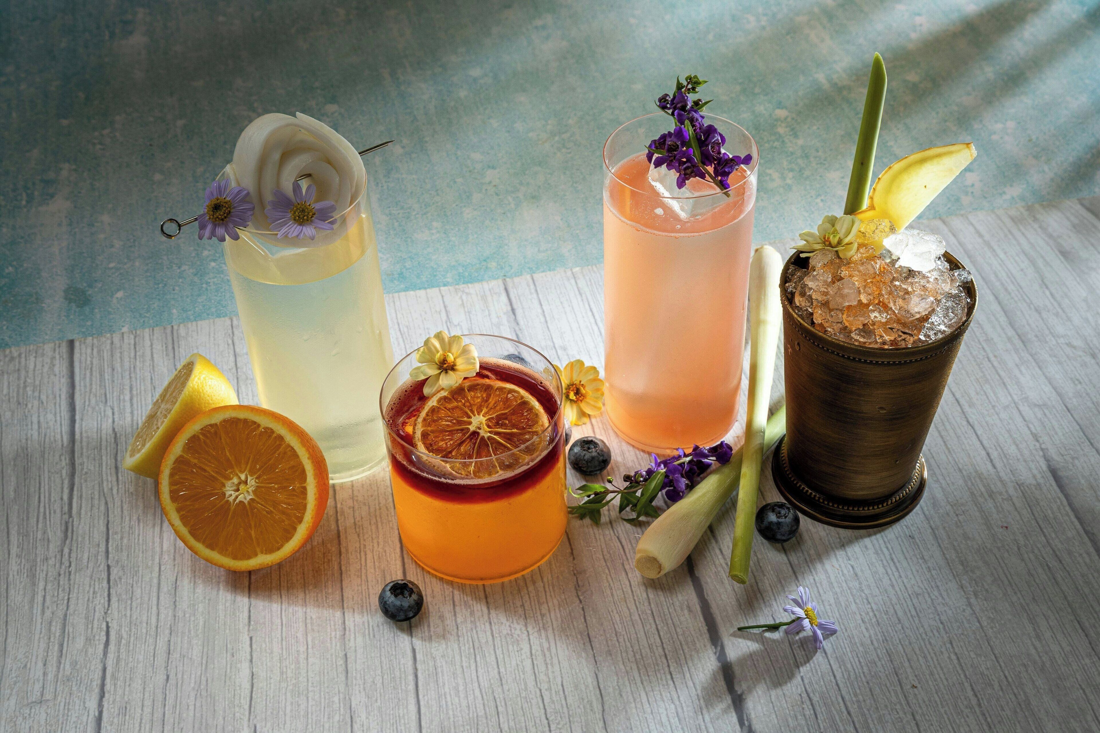 Quatro copos de bebidas com diferentes enfeites e frutas sobre uma superfície de madeira.