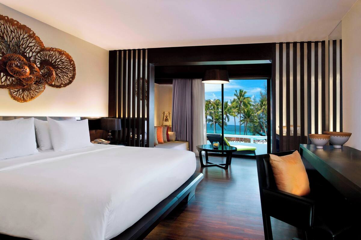 A hotel room with a large bed, a desk, a chair, a view of the ocean, and a decorative wall piece.