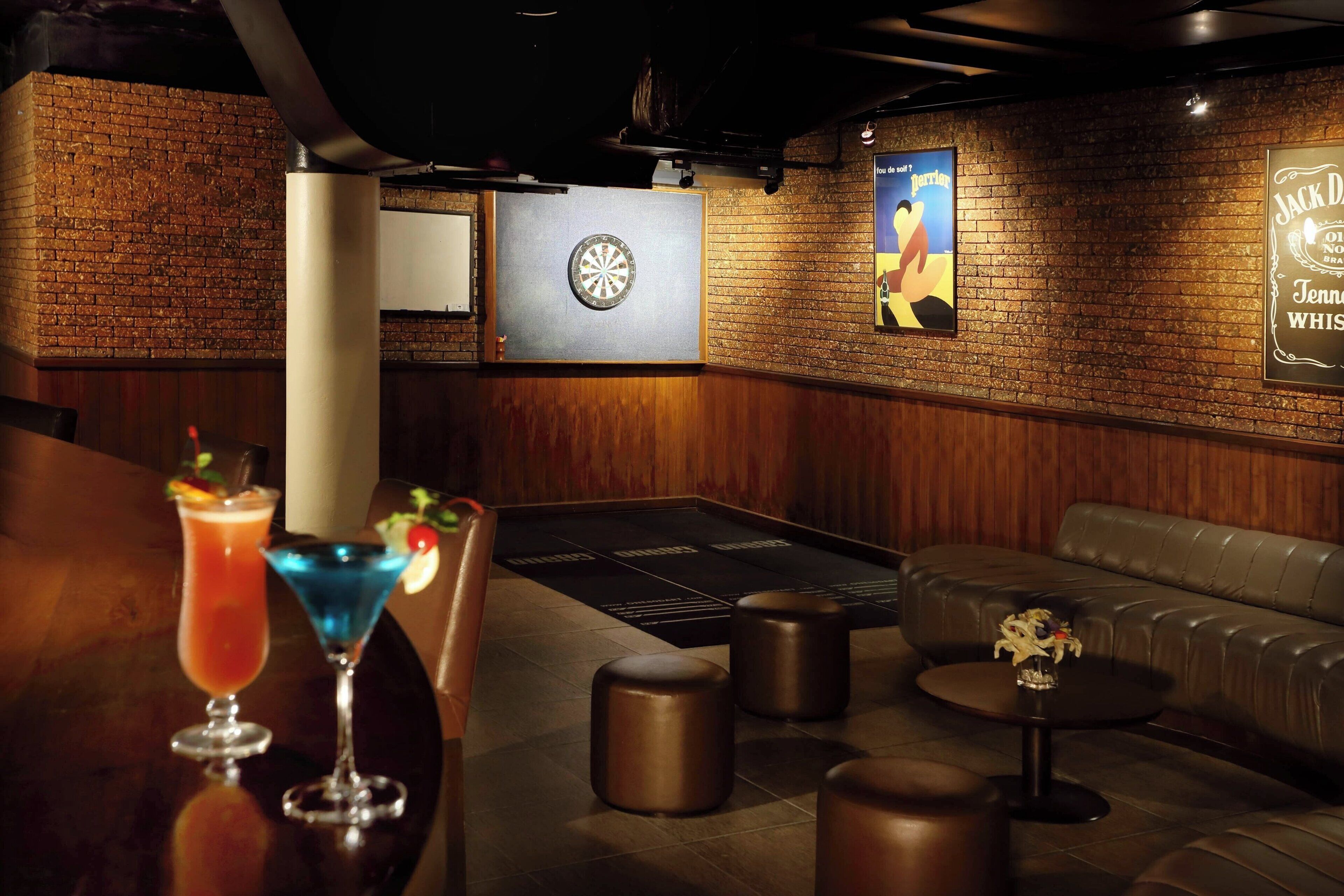 Espaço de bar com dardos, um sofá e banquetas.