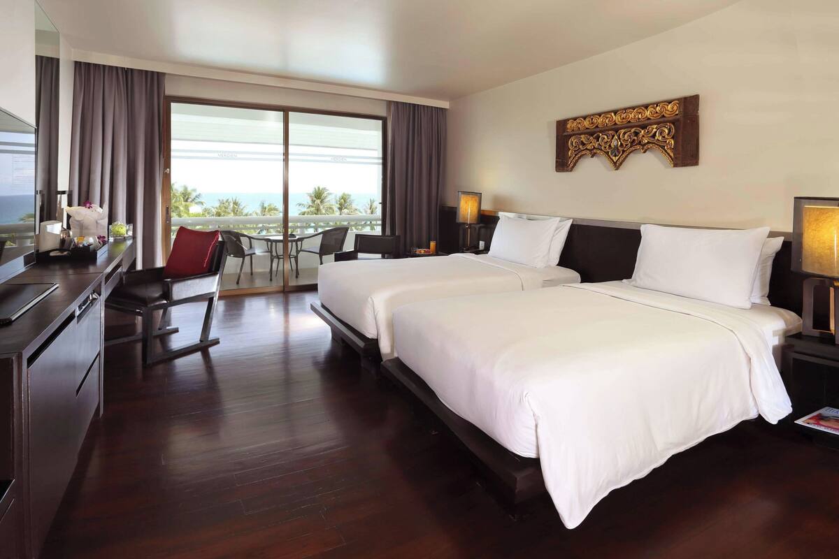 A hotel room with a large bed, a desk, a chair, and a balcony with a view of the ocean.