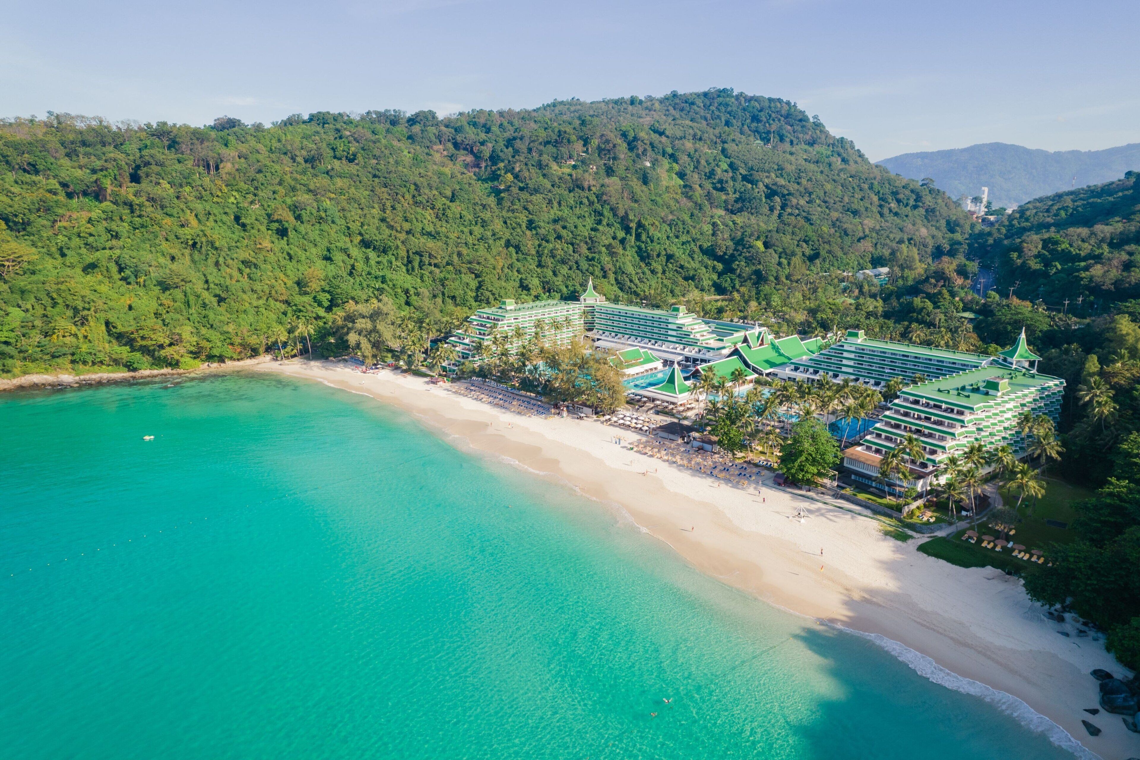 A resort with multiple green-roofed buildings, a beach, and a forested hillside.