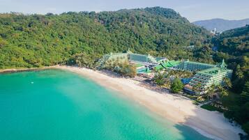 A resort with multiple green-roofed buildings, a beach, and a forested hillside.