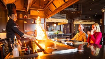 A chef preparing food at a counter with a customer and a server.