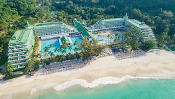 Vista aérea de un complejo turístico con varias edificaciones, una piscina grande y una zona de playa.
