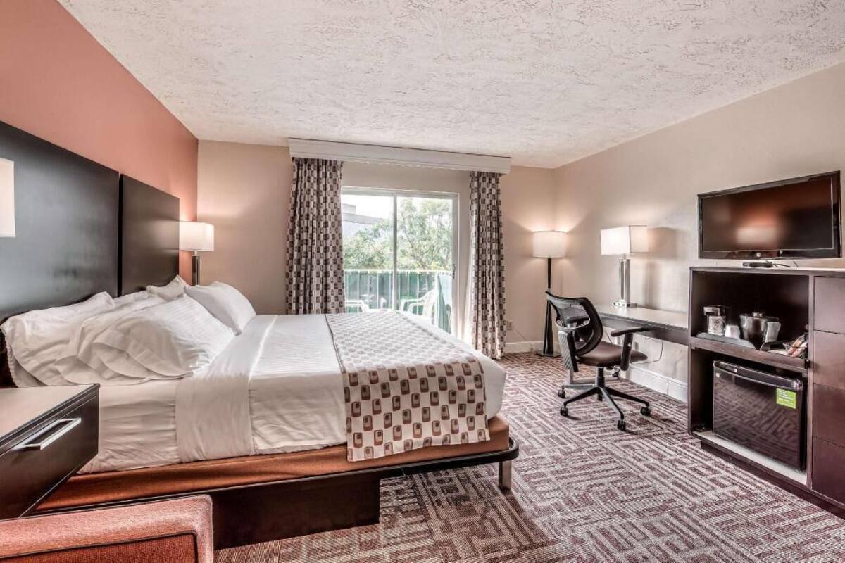 A hotel room with a bed, desk, chair, television, and a balcony with curtains.
