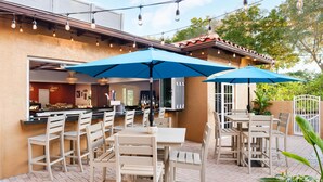 An outdoor patio with white chairs and tables, blue umbrellas, and string lights.