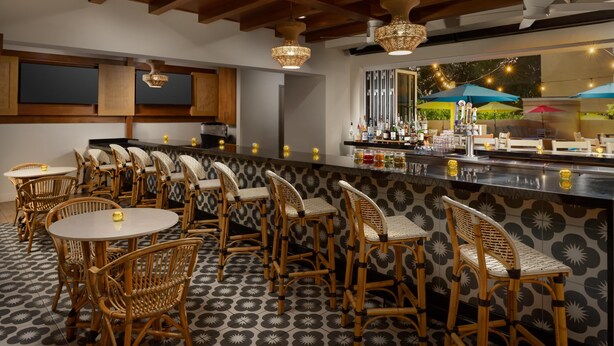 A bar area with wicker chairs, a counter with bottles, and string lights.