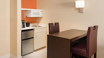 Une cuisine compacte équipée d’un four à micro-ondes, d’une machine à café et d’un réfrigérateur, ainsi qu’une table à manger avec deux chaises et un luminaire fixé au mur.