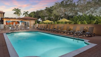 Una piscina al aire libre, sombrillas, sillones reclinables de piscina