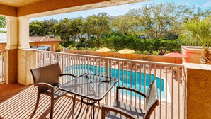 A balcony with a pool, wicker furniture, and a view of the surrounding greenery.