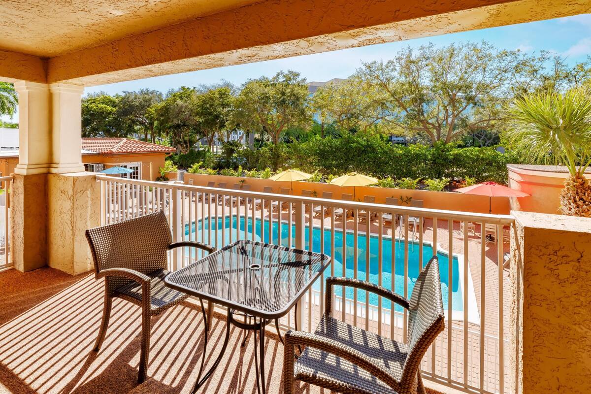 A balcony with a pool, wicker furniture, and a view of the surrounding greenery.
