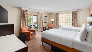 A hotel room with a bed, a desk, an orange chair, and a view of the outdoors.