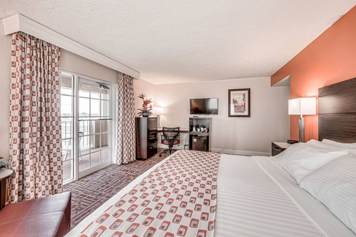 A hotel room with a large bed, a desk, a chair, a TV, and a window with curtains.