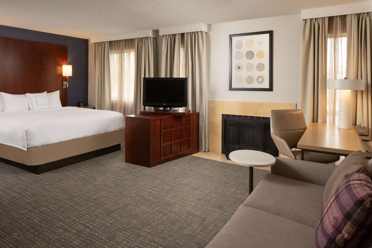 Une chambre d’hôtel avec un grand lit, une télévision, une cheminée, un canapé et une petite table.