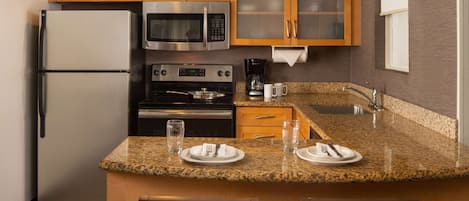 A modern kitchen with granite countertops, stainless steel appliances, wooden cabinets, and a built-in island with seating.