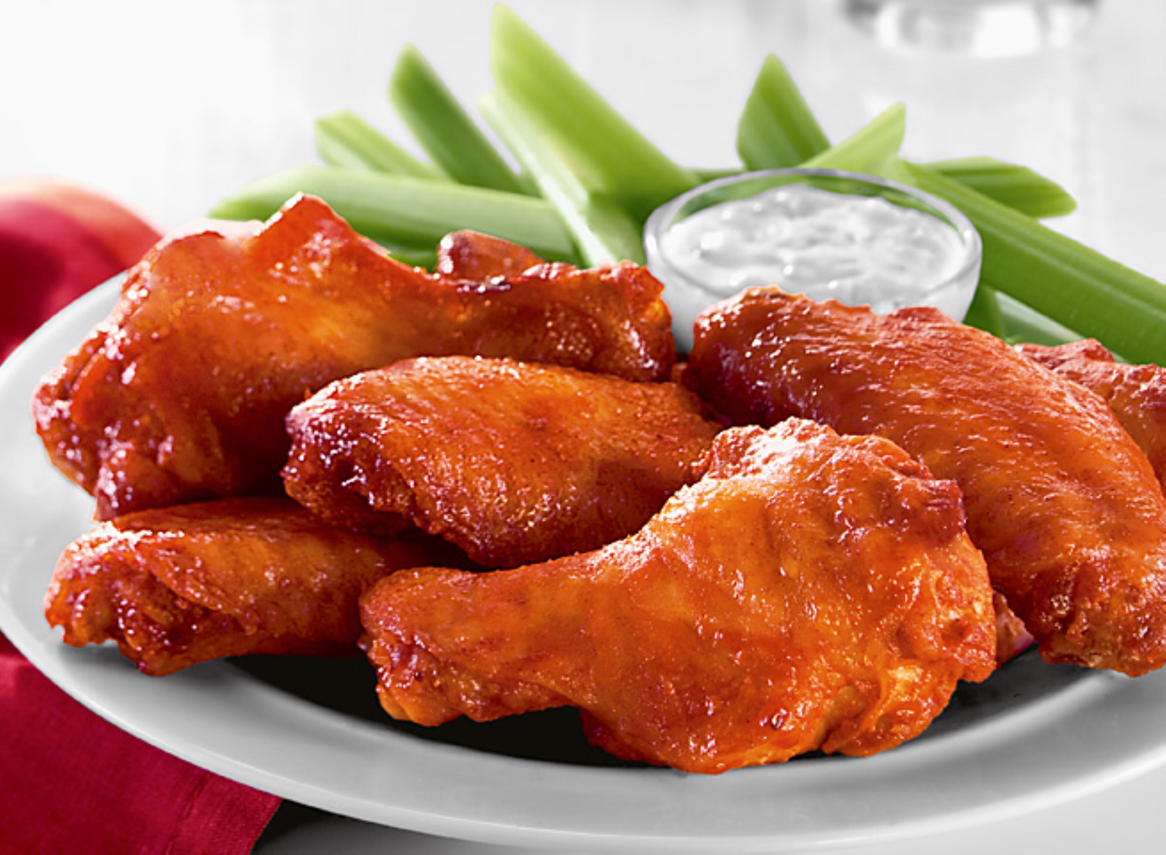 A plate of chicken wings with celery sticks and a small bowl of dip.