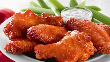 A plate of chicken wings with celery sticks and a small bowl of dip.
