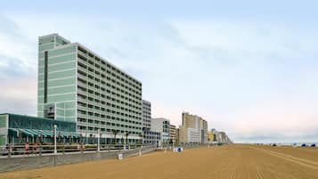 A beachfront hotel with multiple floors, a sandy beach in the foreground, and a clear sky.