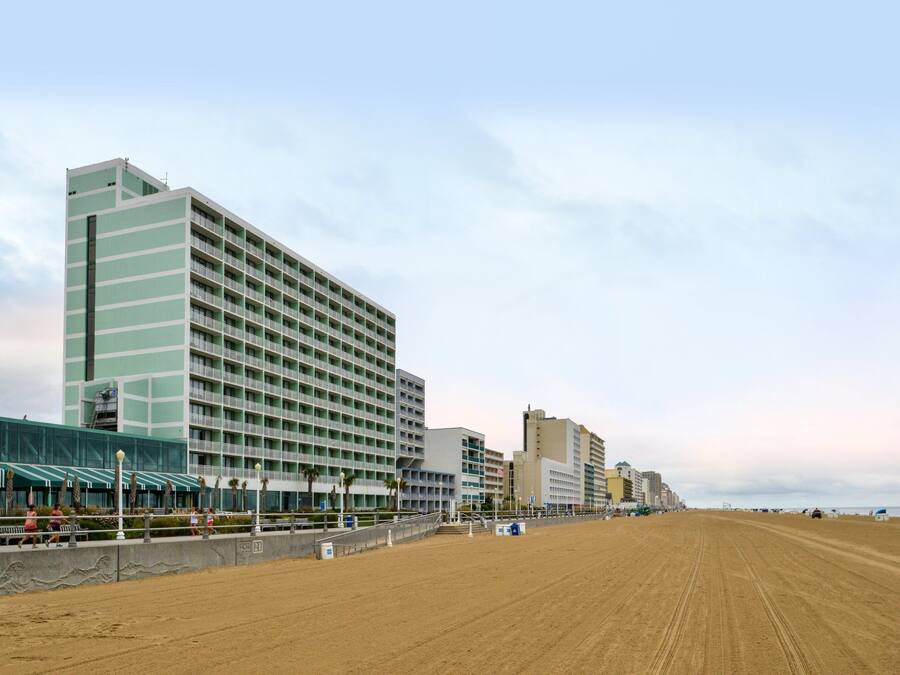 A beachfront hotel with multiple floors, a sandy beach in the foreground, and a clear sky.