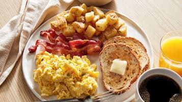 A plate with scrambled eggs, bacon, roasted potatoes, toast with butter, and a glass of orange juice.